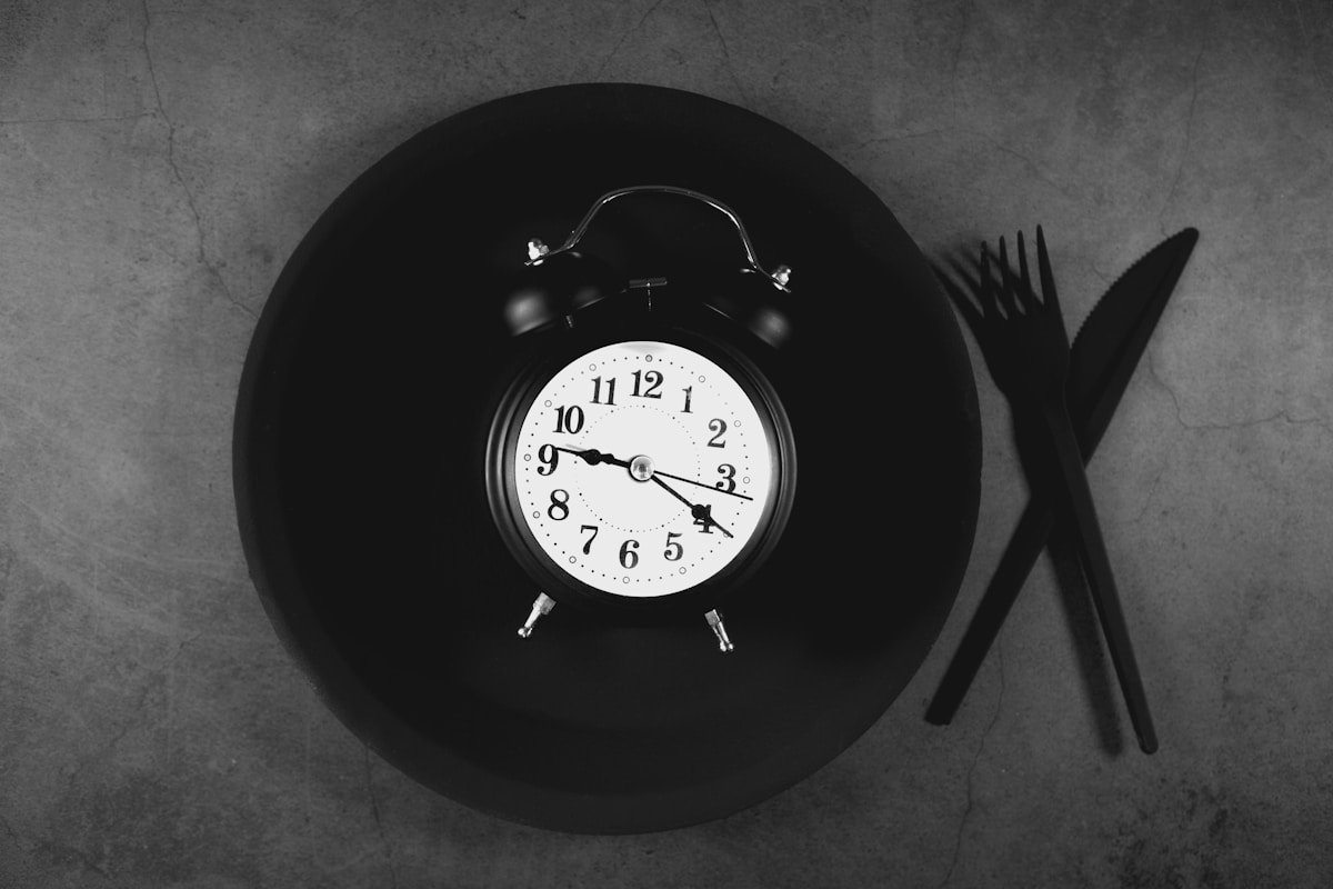 Alarm clock on plate with cutlery symbolizing eating window and fasting schedule